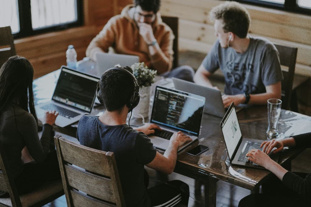 Een groep developers die met laptops aan een houten tafel werkt